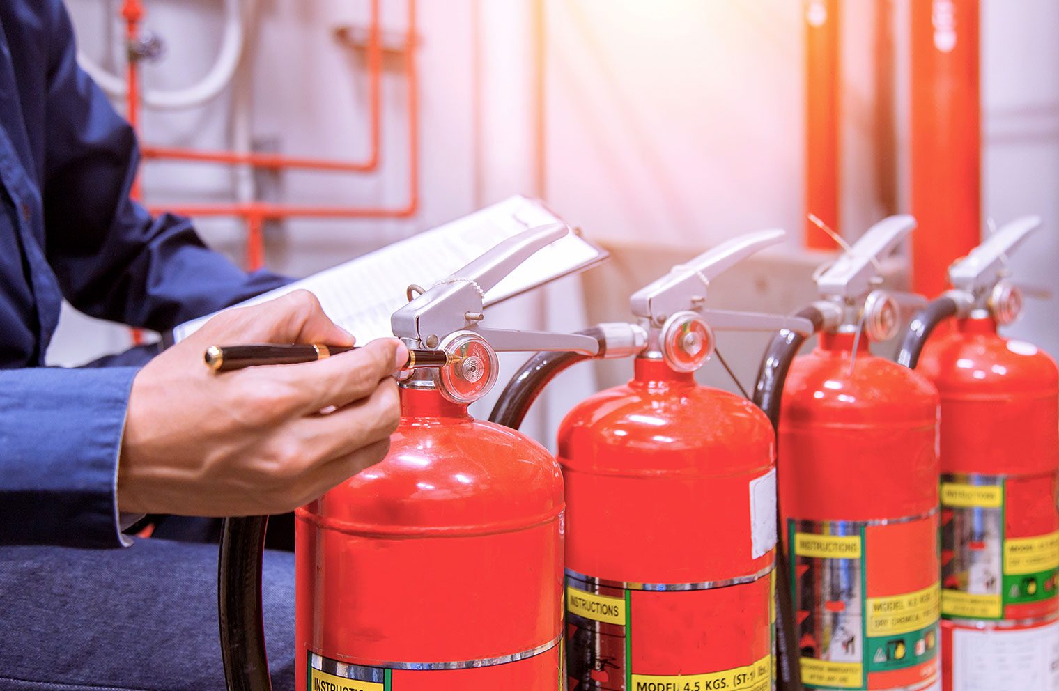 Image of person inspecting row of fire extinguishers with pen and paper in hand.